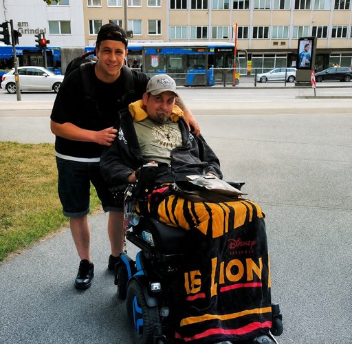 Zwei Freunde, einer im Rollstuhl, gemeinsam unterwegs in der Stadt